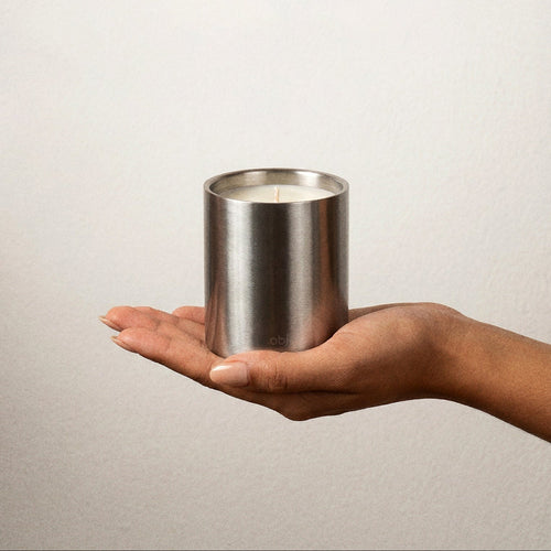 Hand holding a stainless steel cylindrical candle container against a plain background